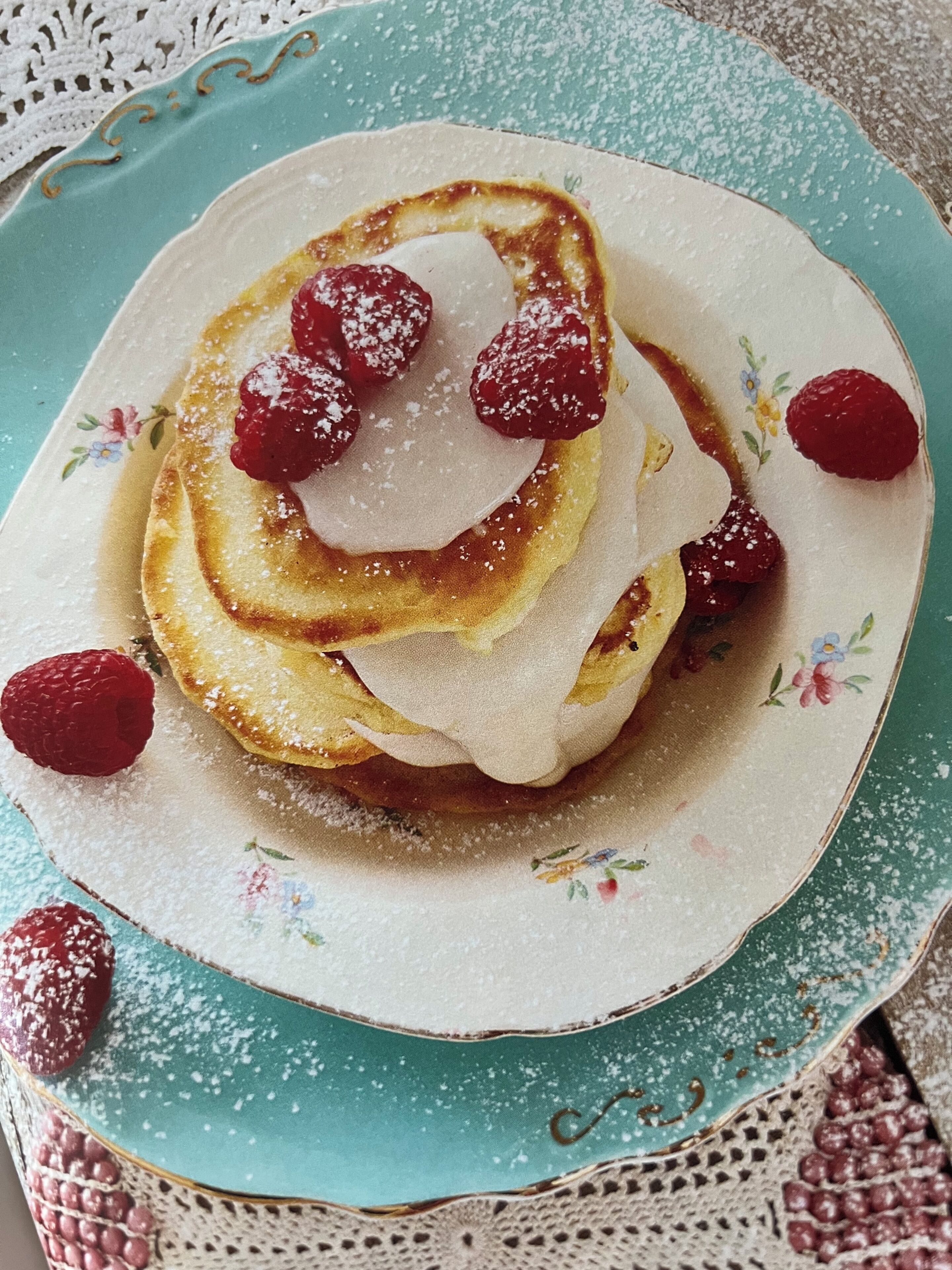 A plate of pancakes with raspberries and powdered sugar.