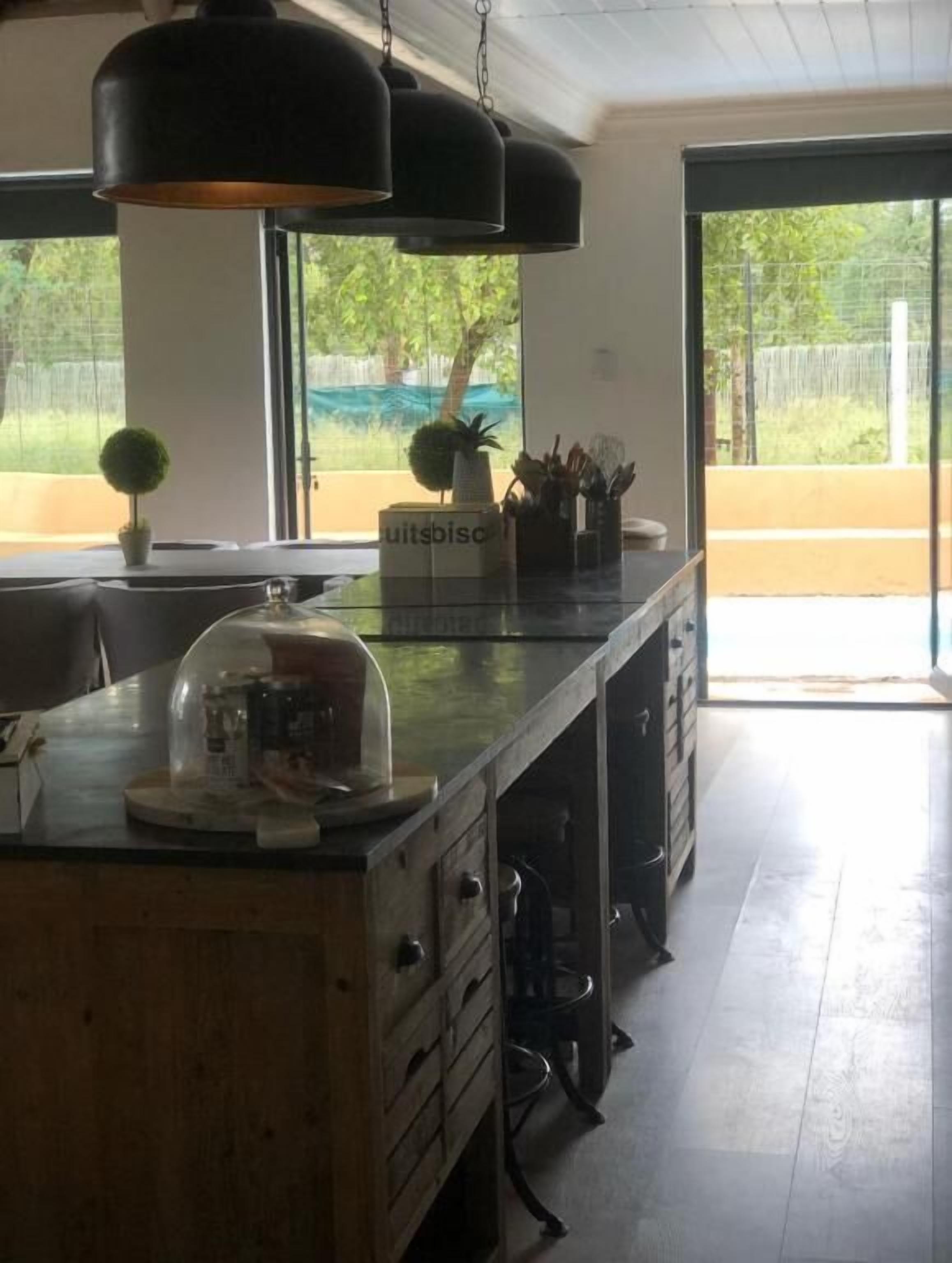 A kitchen with a wooden countertop, a glass-top island, a black pendant light, and a view of greenery outside.