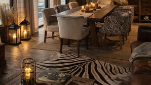 Un comedor con una mesa preparada para cuatro, sillas con estampado de cebra, una gran escultura con forma de cabeza de animal y un techo de madera rústica.