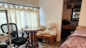 Un dormitorio con una cama, un escritorio con silla, un osito de peluche y una ventana con cortinas.