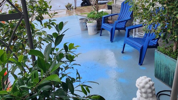 Un espacio al aire libre techado con sillas azules, plantas en macetas y una escultura de piedra.