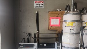 Un lavadero con lavadoras industriales, un cartel de advertencia sobre cámaras de seguridad y grandes tanques de almacenamiento.
