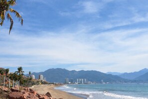 Una playa con cielo despejado, palmeras y montañas al fondo.