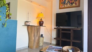 Un saló amb televisió, una làmpada, una taula de cafè amb un diari, una planta i una estant penjada a la paret.