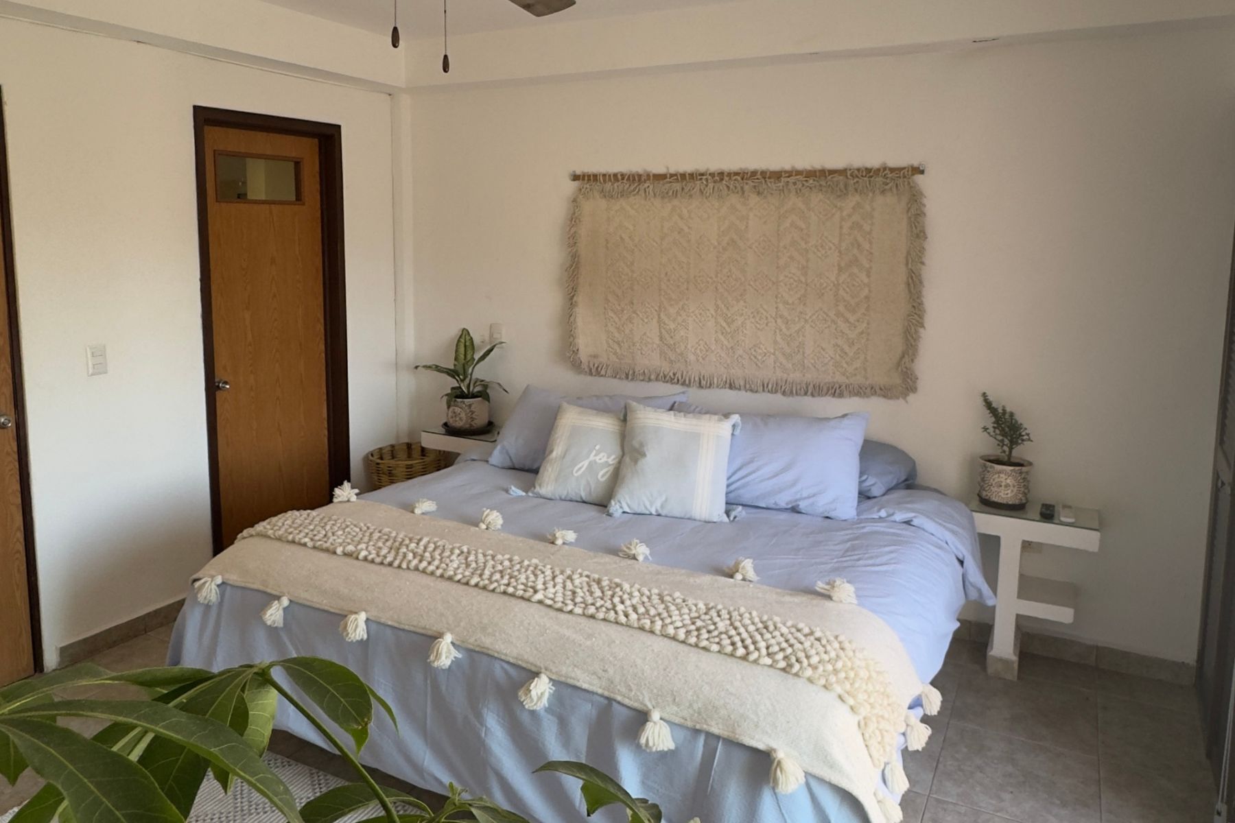 A bedroom with a bed, bedside tables, a door, and a wall-mounted tapestry.