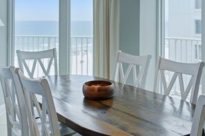 Ein Holzespeisetisch mit einer Schüssel, weißen Stühlen und Blick auf das Meer durch große Fenster.