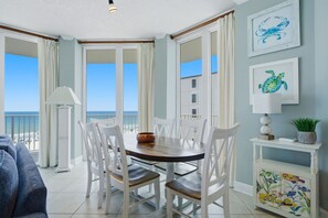 Un coin repas avec une table ronde, des chaises blanches, une lampe et une vue sur l’océan.