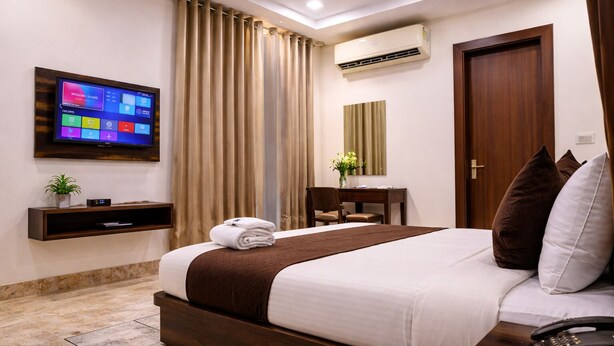 Une chambre d’hôtel équipée d’un lit, d’un téléviseur fixé au mur, d’un bureau avec une chaise, d’un miroir et d’un appareil de climatisation.