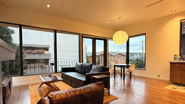 Un amplio espacio de sala con un gran ventanal, un sofá, una mesa de comedor y una zona de cocina.
