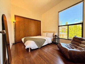 A bedroom with a bed, a wooden wardrobe, a window with a view, and a brown leather sofa.