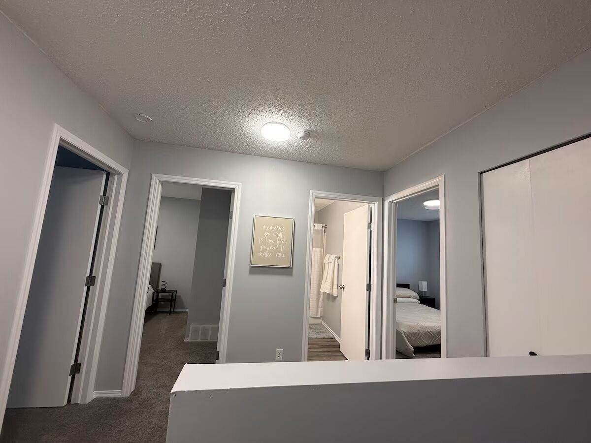 A hallway leading to a bedroom with a bed, a bathroom, and a small sitting area.