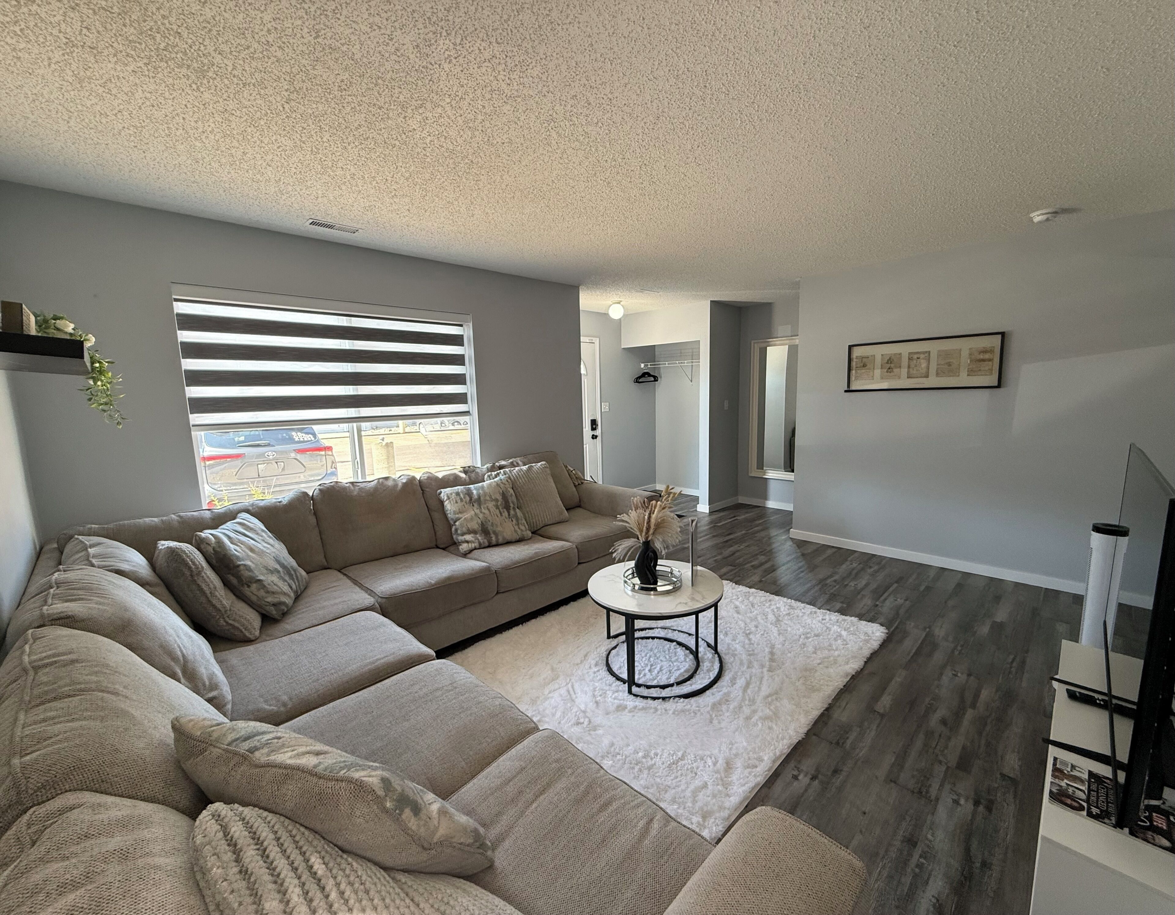A modern living room with a sectional sofa, a round coffee table, and a large window with blinds.