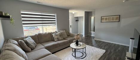 A modern living room with a sectional sofa, a round coffee table, and a large window with blinds.