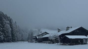 A rustic cabin with a snow-covered roof and a chimney, surrounded by a forest.
