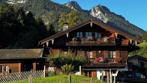 Een klassiek houten chalet met balkon, omgeven door een houten hek en met een berg op de achtergrond.
