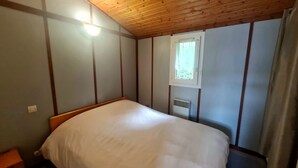 Un dormitorio con techo de madera, una cama individual, una ventana con vistas y un respiradero en la pared.