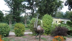 Ein Garten mit einer Skulptur, verschiedenen Pflanzen und einem Gebäude im Hintergrund.