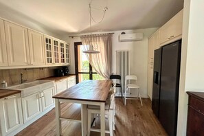 Eine Küche mit Holzboden, weißen Schränken, einem Esstisch, einem Kühlschrank und einem Fenster mit Vorhängen.