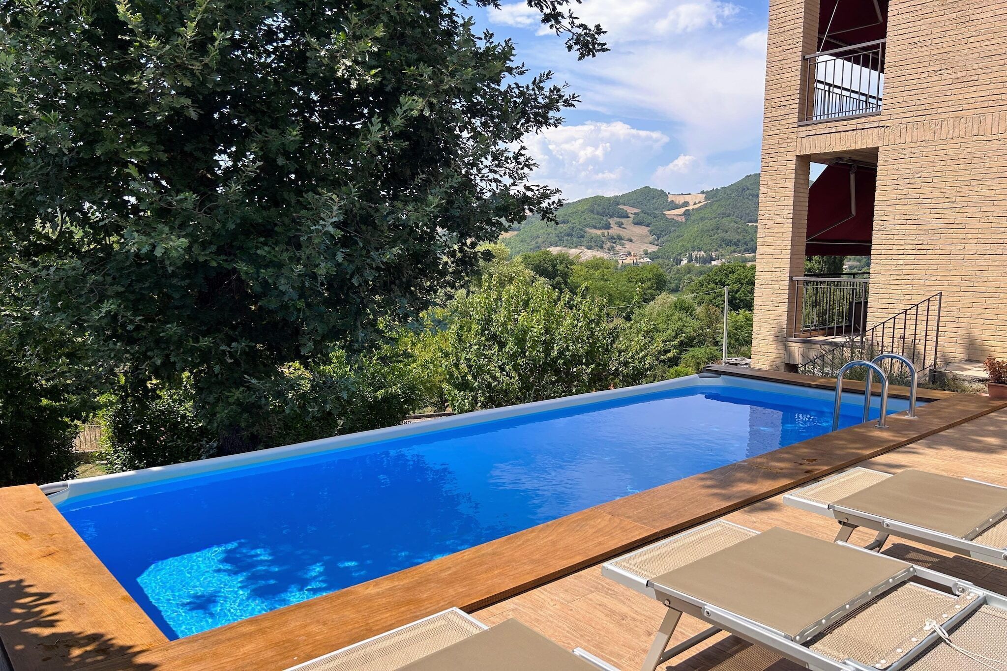 Une piscine dotée d’une terrasse en bois et de chaises longues, entourée d’arbres et offrant une vue sur les collines.