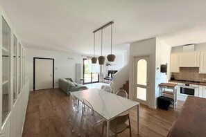 Eine moderne Küche mit weißen Schränken, einem Esstisch mit Stühlen und einer Treppe, die in ein weiteres Geschoss führt.