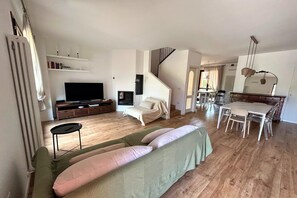 Een moderne woonkamer met een flatscreen televisie, een bank, een eethoek met een tafel en stoelen, en een trap die naar een hoger niveau leidt.