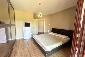 Ein Schlafzimmer mit einem Bett, einer Kommode, einem Fernseher auf der Kommode und einer Tür zu einem anderen Raum.