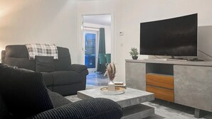 Ein modernes Wohnzimmer mit einer Couch, einem Couchtisch, einem Fernseher und einer kleinen Pflanze.