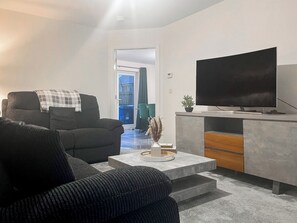 Ein modernes Wohnzimmer mit einer Couch, einem Couchtisch, einem Fernseher und einer kleinen Pflanze.