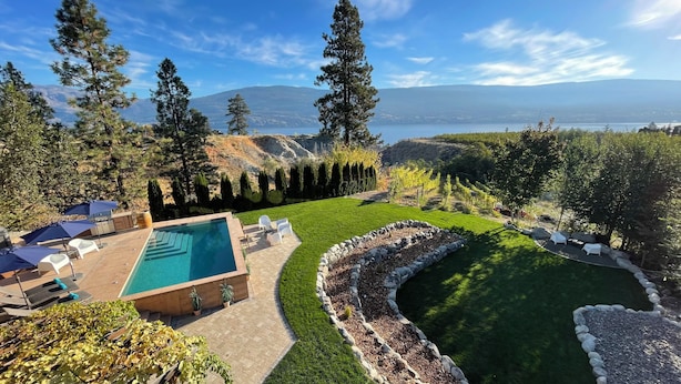 A pool with a stone border, a patio with chairs, and a view of mountains and a lake. - Summerland Lakeview Vineyard with Pool (Summerland)