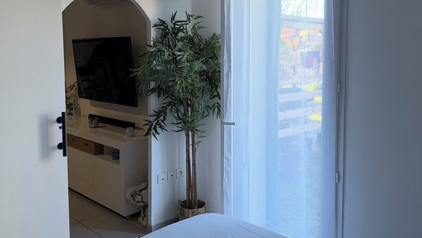 Makuuhuoneessa on sänky, televisio, huonekasvi ja ovi, joka johtaa parvekkeelle.