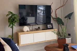 Ein Wohnzimmer mit Flachbildfernseher an der Wand, einem Holzschrank darunter und zwei Blumentöpfen.