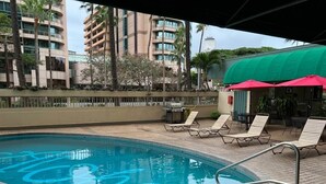 Ein Pool mit Liegestühlen und einem überdachten Bereich, umgeben von hohen Gebäuden.