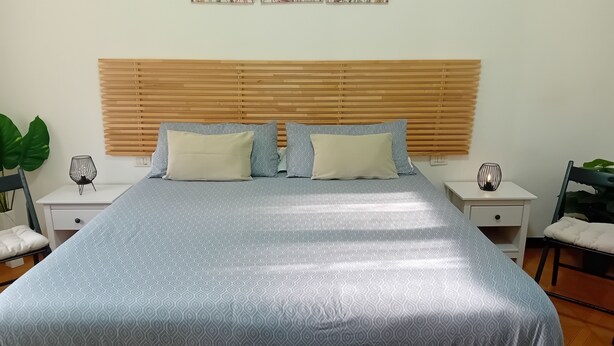 A neatly made bed with a patterned bedspread, two pillows, a wooden headboard, bedside tables with lamps, and a plant. - BGM Apartment Milan Rho Fiera—trains every 15 minutes to Milan (Cesate)