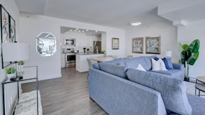 Een moderne woonkamer met een grijze bank, een eethoek en een keuken op de achtergrond.