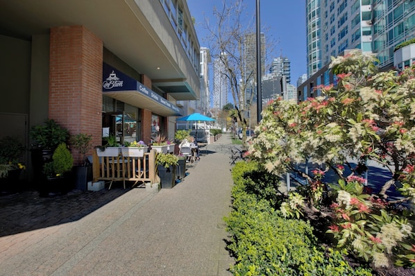 A sidewalk café with outdoor seating, a coffee shop, and a building with a glass facade.