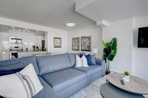 A modern living room with a grey sofa, a round coffee table, and a kitchen in the background.