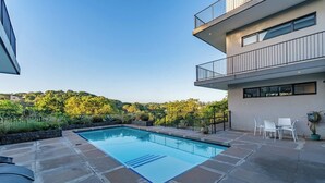 Area piscina moderna all'aperto con vista libera sul paesaggio circostante, patio in pietra e un edificio a più piani con balconi.