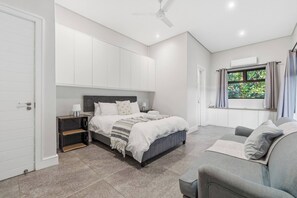 A bedroom with a bed, bedside table, and a window with curtains. - Bay House - Staynest Guesthouse (Ballito)