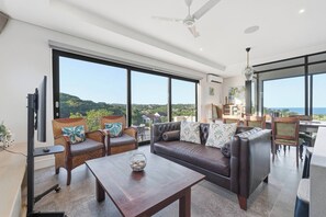 A modern living room with a large window, a sofa, a coffee table, and a television. - Bay House - Staynest Guesthouse (Ballito)