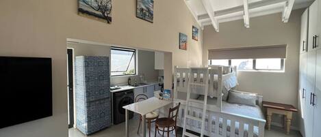 A compact living space with a kitchenette, a dining area, a bunk bed, and a television.