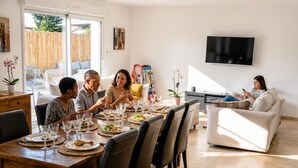 Un coin repas avec une table en bois dressée pour quatre personnes, entourée de chaises, un téléviseur fixé au mur et un canapé en arrière-plan.