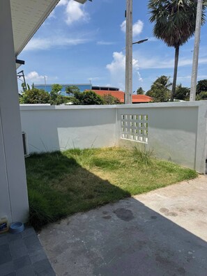 Un espacio al aire libre cubierto con piso de concreto, una pared blanca con ventana de celosía y una palmera.