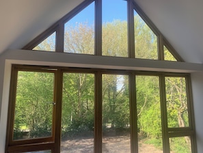 Ein Zimmer mit großen Fenstern, einer geneigten Decke und Blick auf ein bewaldetes Gebiet.
