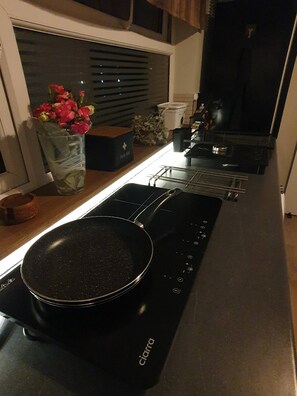 A kitchen with a black stovetop, a pan, a vase with flowers, and a window with blinds.