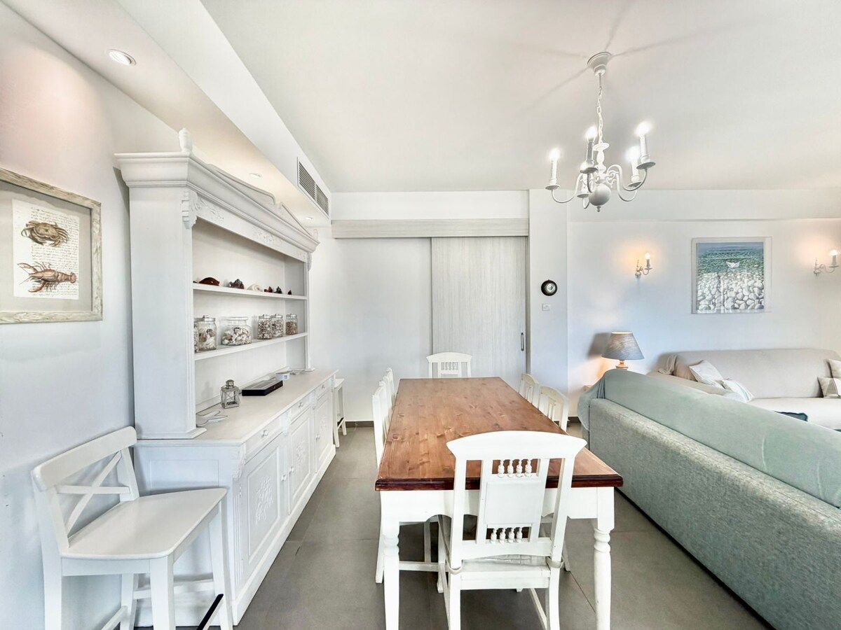 A dining area with a wooden table and white chairs, a white sofa, and a chandelier.