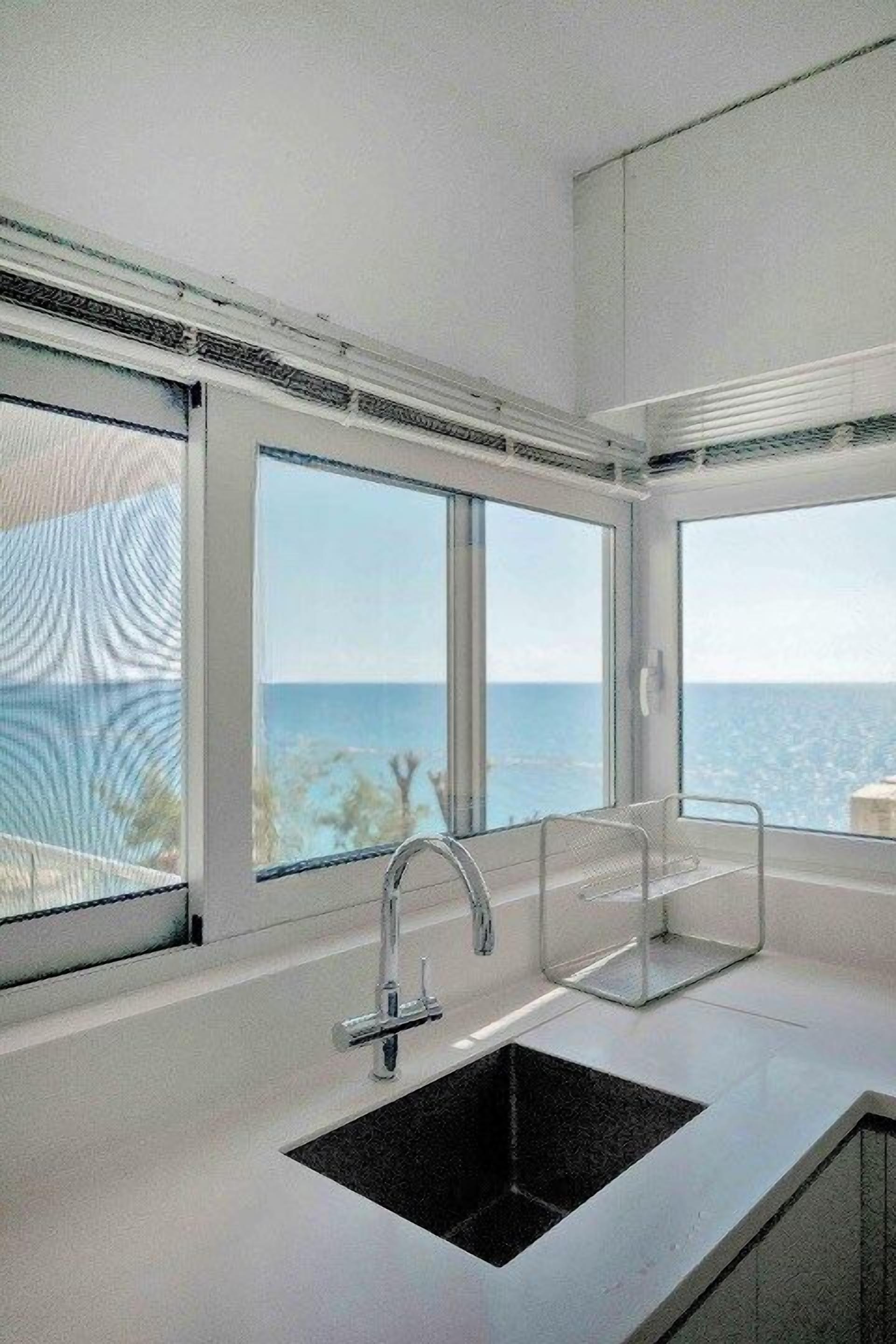 Une cuisine moderne dotée d’un évier noir, d’un robinet en acier inoxydable et de grandes fenêtres offrant une vue sur la mer.