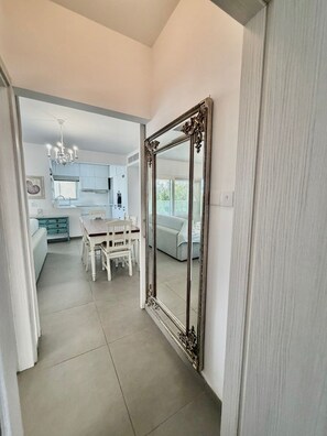 A modern kitchen with white cabinets, a dining table, and chairs. A large ornate mirror is on the wall. - Luxury Beach Front Flat Kyma 3 (Germasogeia)
