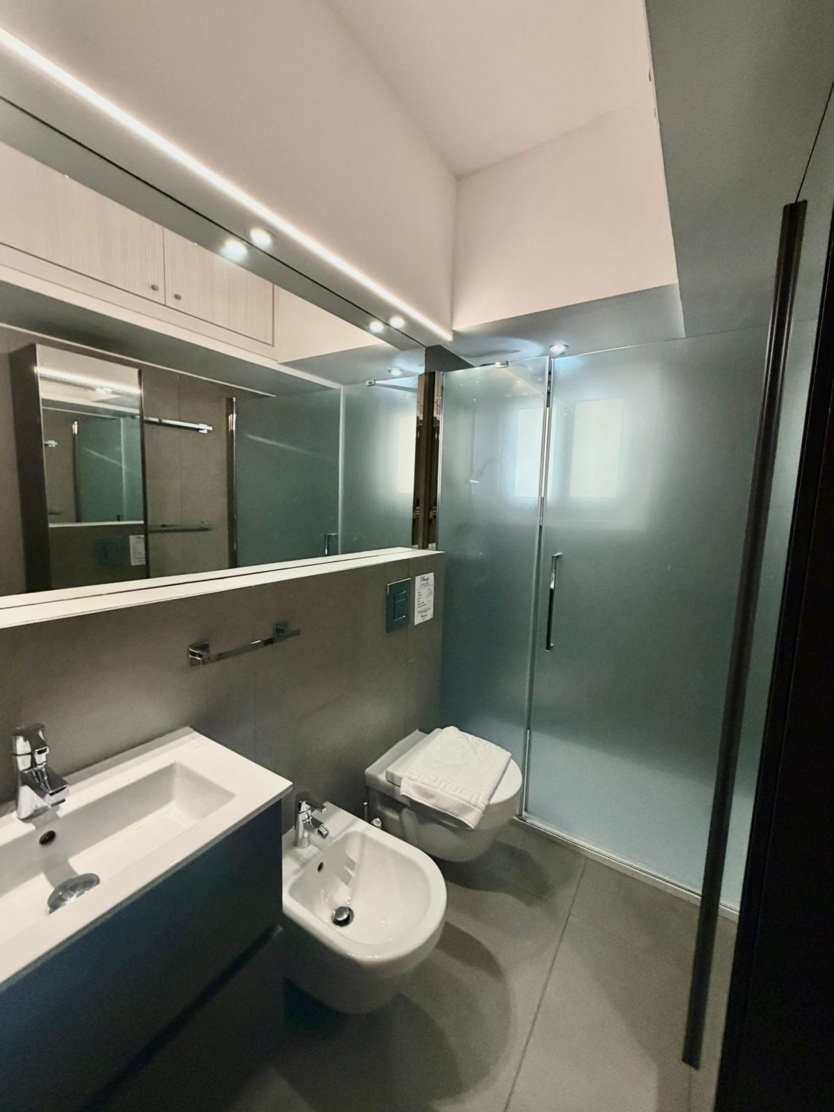A modern bathroom with a large mirror, a sink, a bidet, and a toilet.