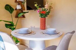 Ein runder Esstisch mit zwei weißen Schüsseln und Tellern, einem Glas und einer Vase mit Blumen.