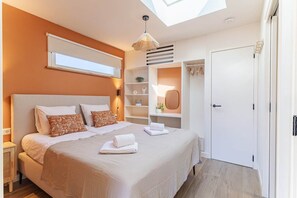 Ein Schlafzimmer mit Bett, Nachttischen, einem Kleiderschrank, einem Dachfenster und einer eingebauten Ablage mit Spiegel.